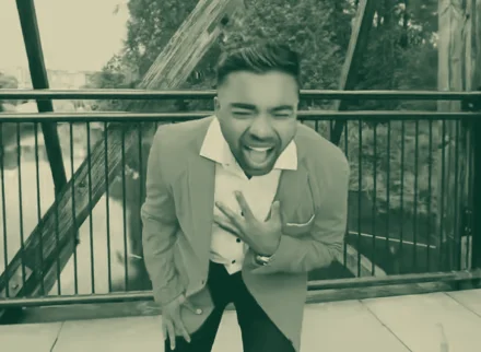 A man in a blazer doubled over, laughing and wincing